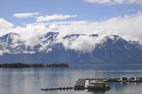 view of a lake with boats in the harbor and a large mountain with clouds around it in the distance. 