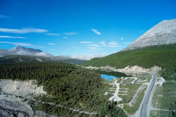 A highway weaving around a mountain with trees and a lake in the background. 